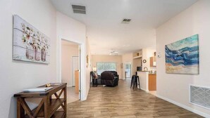 A spacious living area with a herringbone wood floor, a wooden console table, a sofa, and a dining area with a bar. - Sandy Toes Hideaway - Private Pool & Games Room (Clermont)