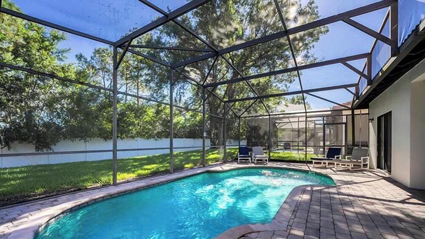 A swimming pool with a glass enclosure, surrounded by a patio area with lounge chairs. - Sandy Toes Hideaway - Private Pool & Games Room (Clermont)