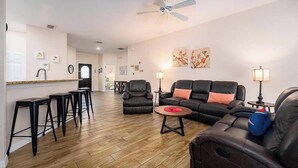 A spacious living room with a black leather sofa, a coffee table, and a dining area with a bar stool. - Sandy Toes Hideaway - Private Pool & Games Room (Clermont)