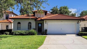 A two-story house with a red-tiled roof, a white garage door, and a well-maintained lawn. - Sandy Toes Hideaway - Private Pool & Games Room (Clermont)