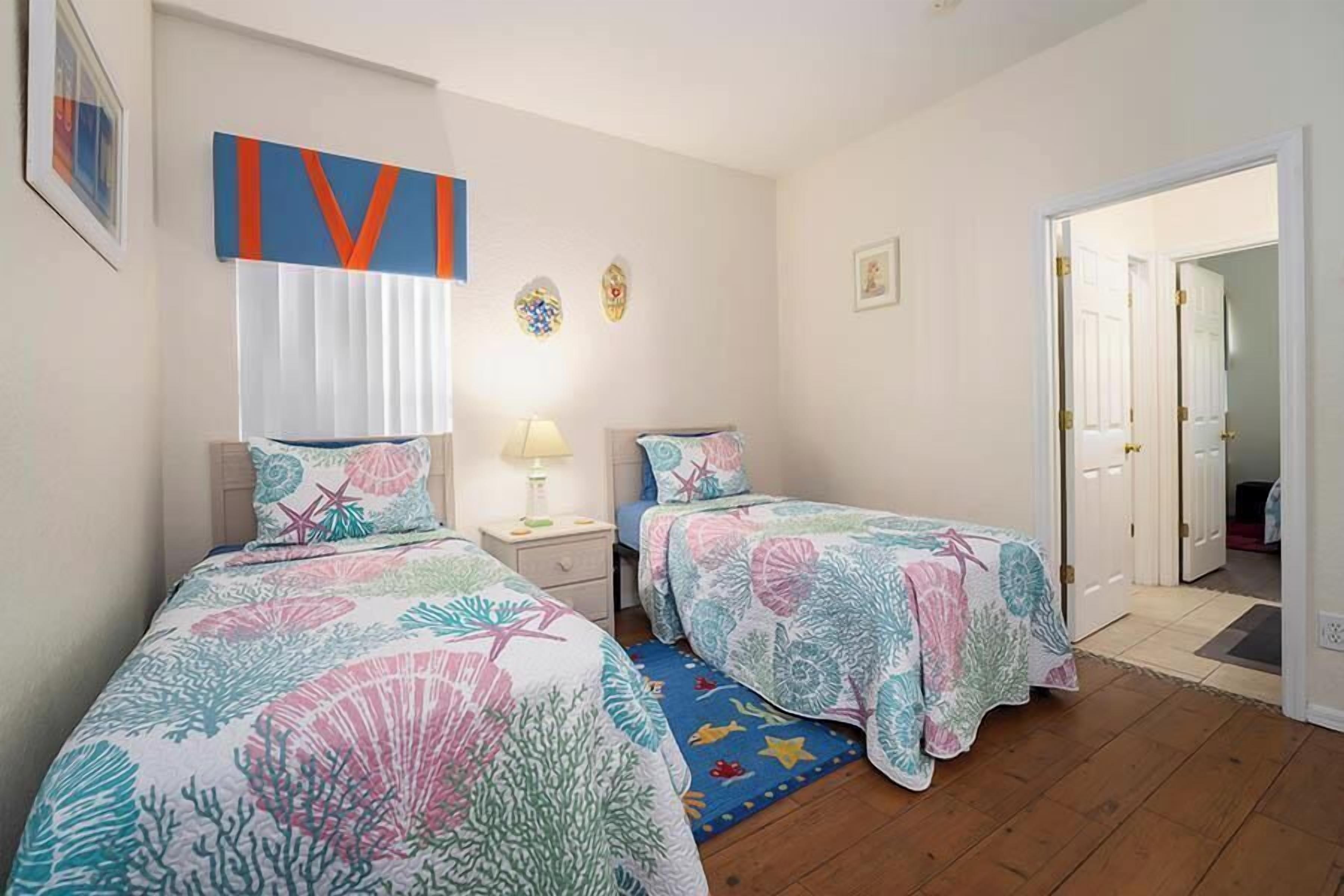 Un dormitorio con dos camas, una mesita de noche, una lámpara y una puerta que da a otra habitación.