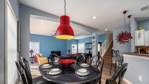 Uma área de refeições com uma mesa preta para quatro pessoas, rodeada por cadeiras pretas. Uma luminária pendente vermelha paira sobre a mesa.