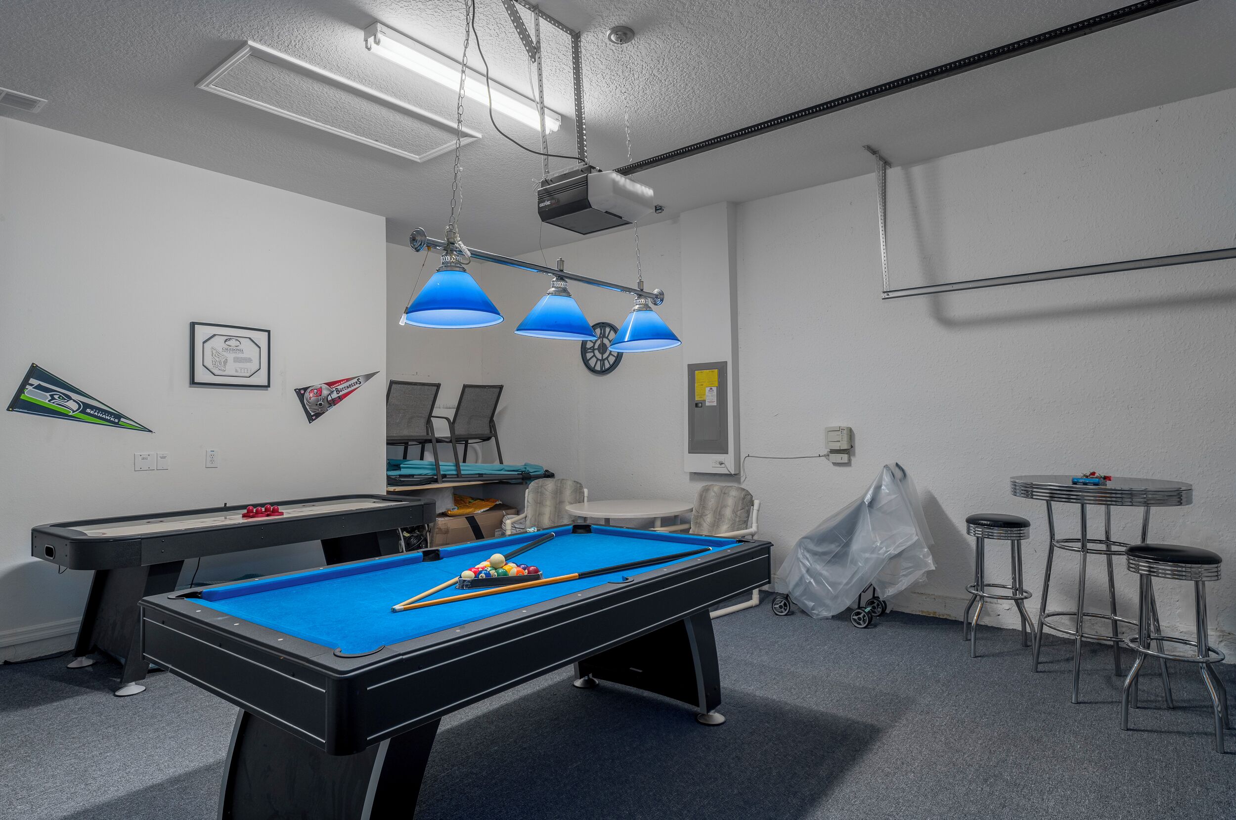 Une table de billard recouverte de feutre bleu, avec un éclairage suspendu et un projecteur.