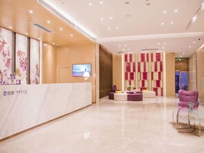 A hotel reception area with a marble counter, a television, and a seating area with purple and white chairs. - Lavande Hotel (Shenzhen)