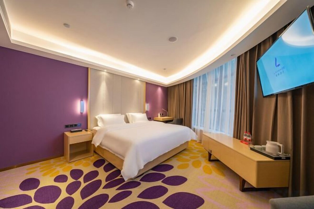 A hotel room with a large bed, a flat-screen TV, a desk, and a seating area.