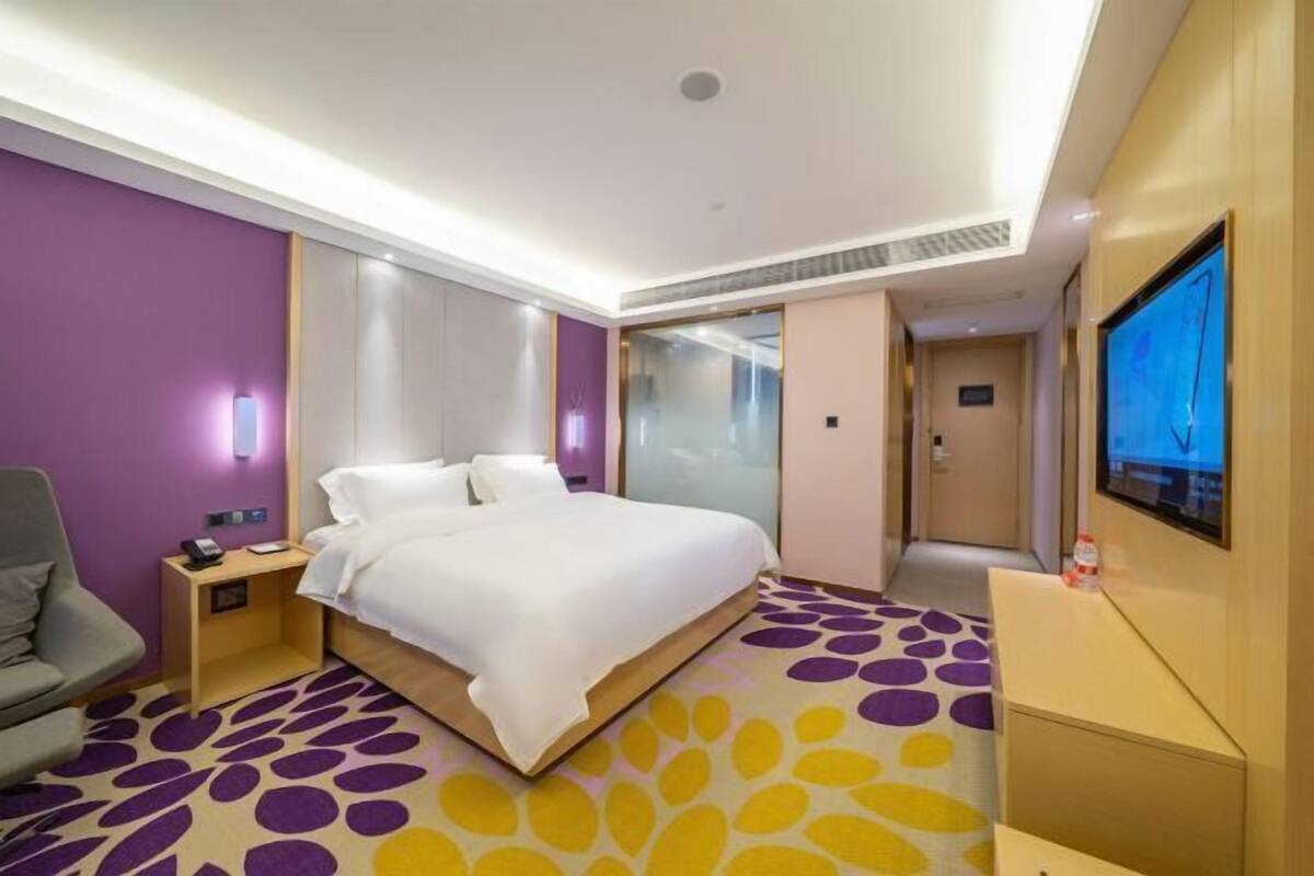 A hotel room with a bed, a desk, a chair, a TV, and a bathroom.