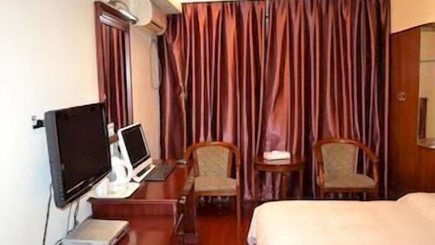 A hotel room with a bed, a desk with a laptop, a chair, a television, and a curtain. - Lavande Hotel (Shenzhen)