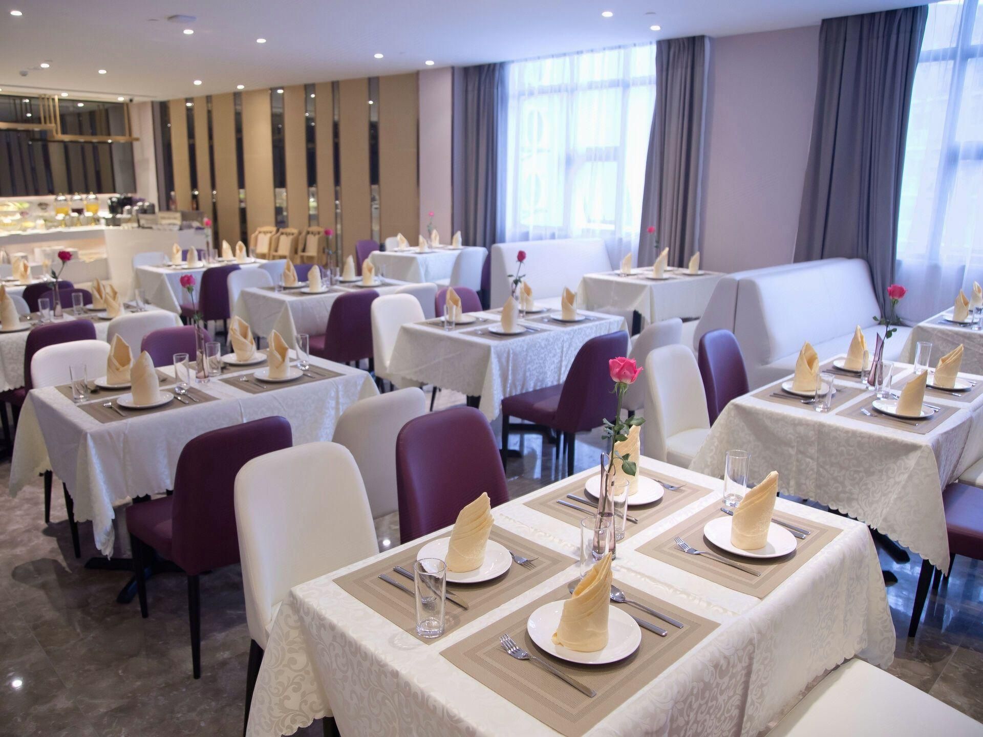 A hotel dining area with multiple tables set for guests, featuring white tablecloths and napkin rings.