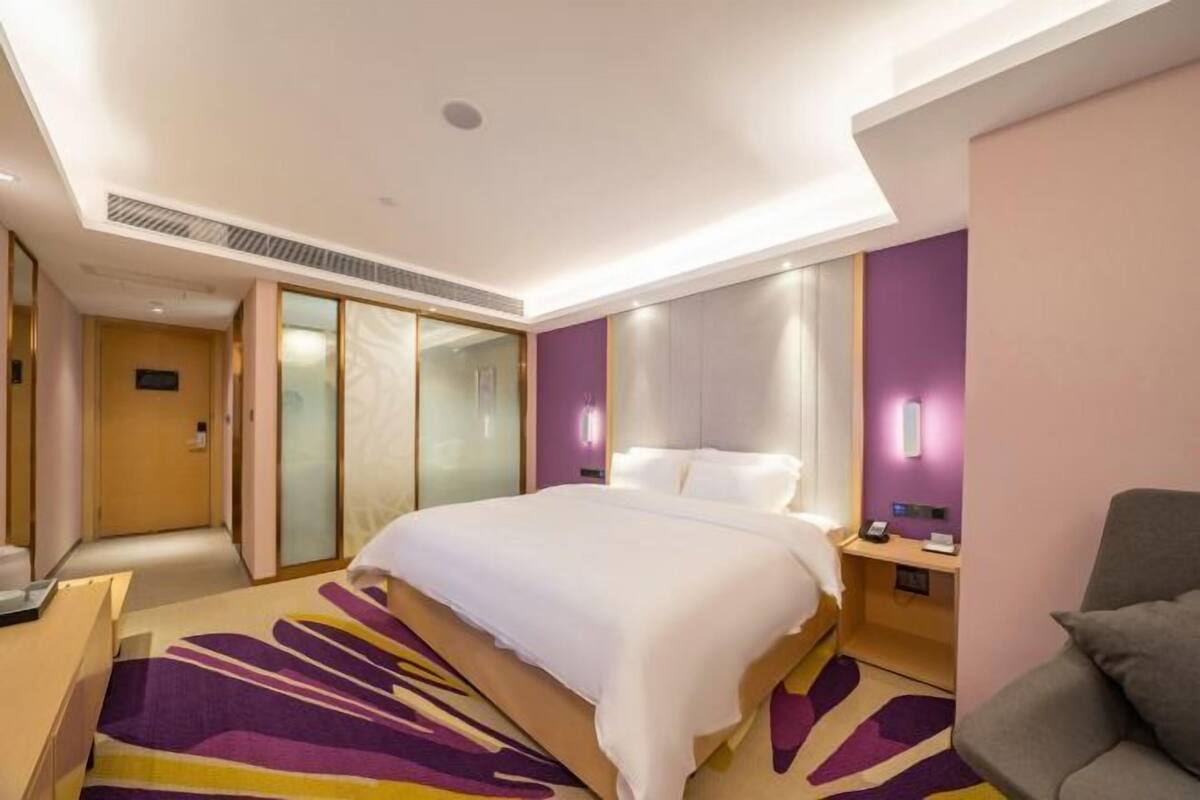 A modern hotel room with a bed, bedside table, and a desk with a chair.