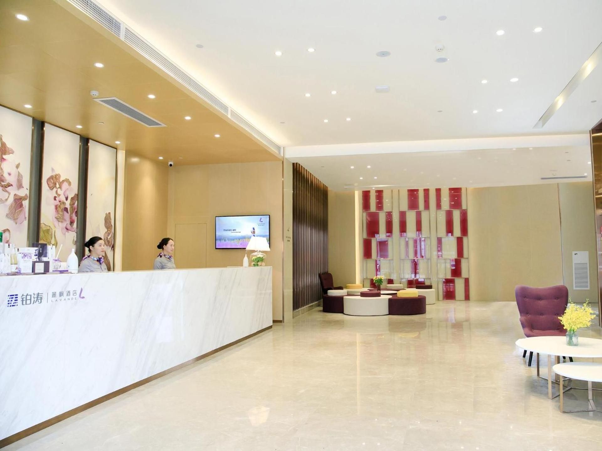A hotel reception area with a marble counter, a television screen, and a seating area with red and white decor.