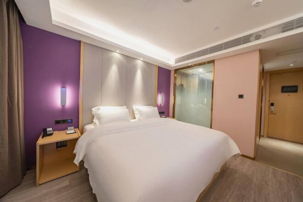 A hotel room with a bed, bedside table, and a mirror.