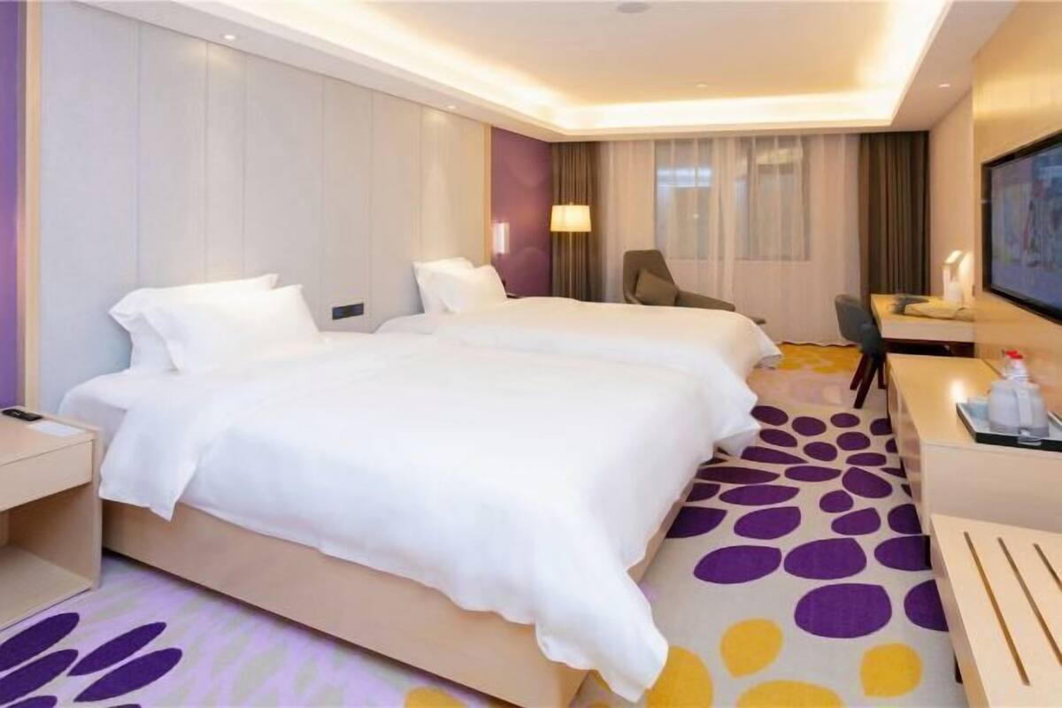 A hotel room with two beds, a desk, a chair, and a TV.