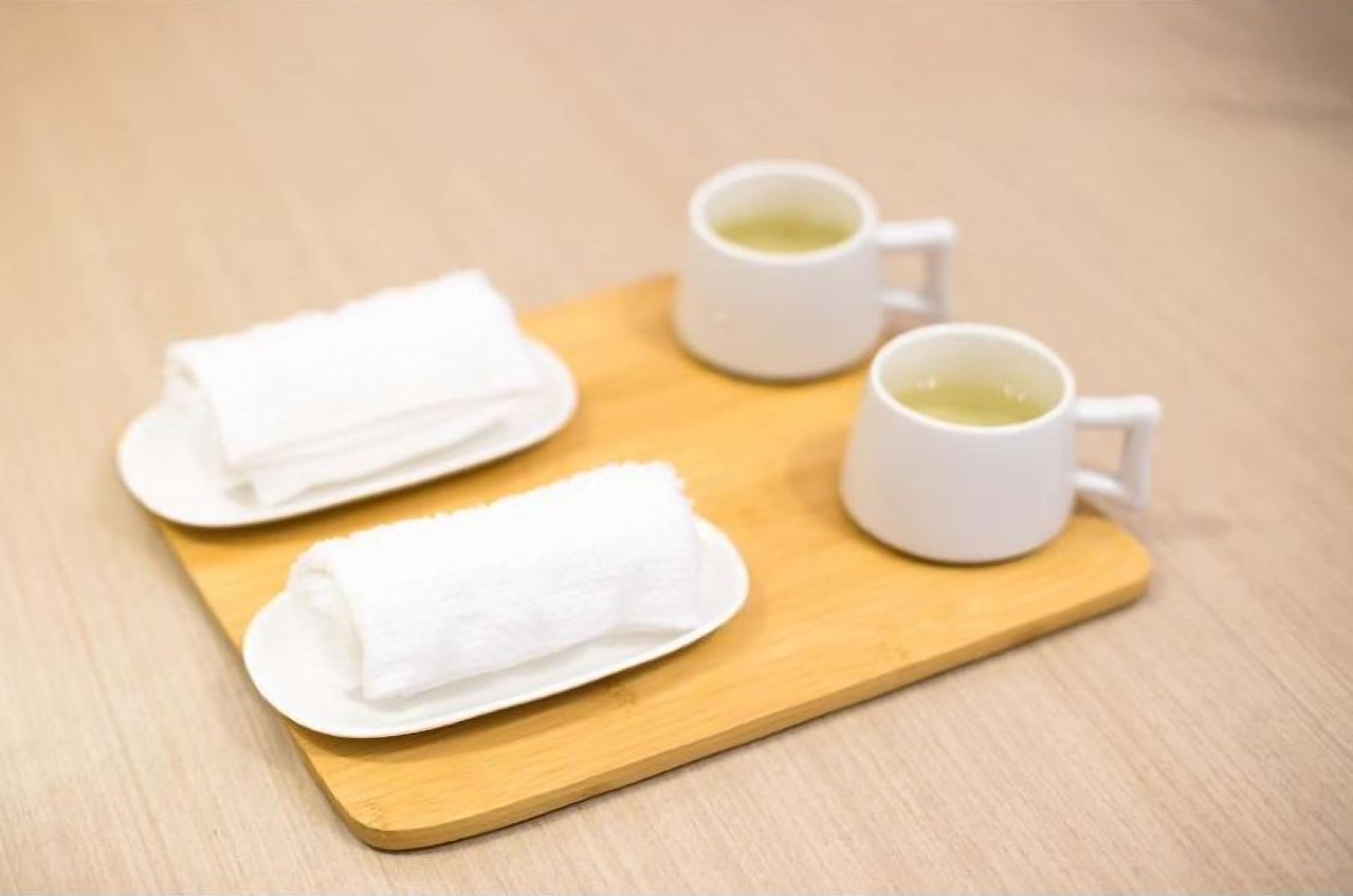 A tray with two white towels and two white mugs on a wooden surface.