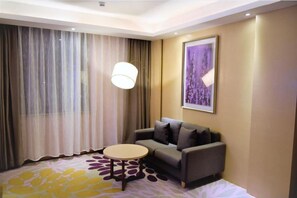 A hotel room with a sofa, a round table, a lamp, a large window with curtains, and a framed picture on the wall. - Lavande Hotel (Shenzhen)