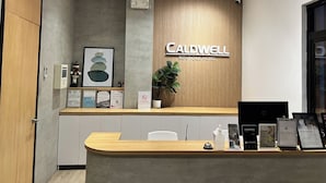 Un mostrador de recepción con un cartel que indica 'Caldwell Boutique Hotel', un letrero de 'No Fumar', certificados enmarcados y un terminal de pago digital.