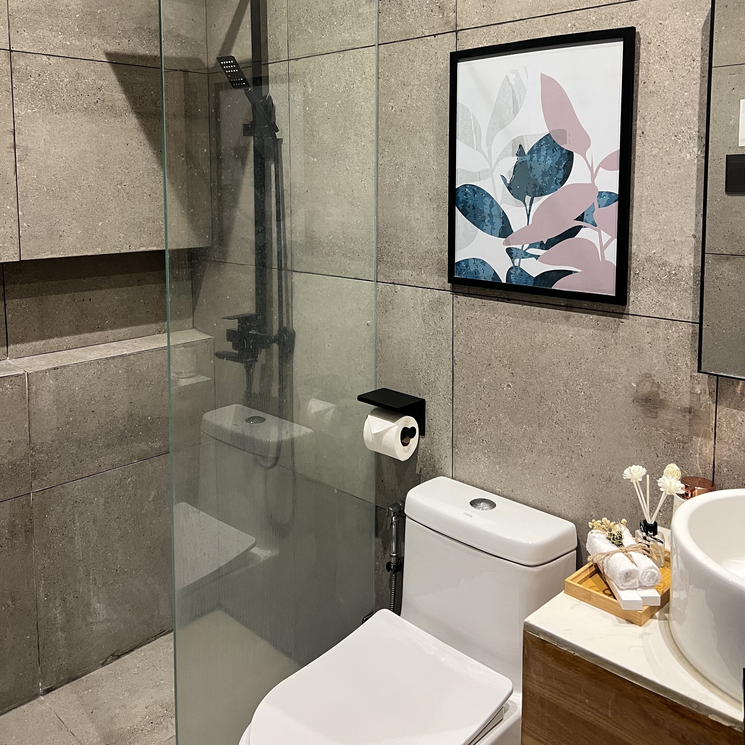 A modern bathroom with a glass shower enclosure, a toilet, and a sink with a wooden tray holding toiletries.