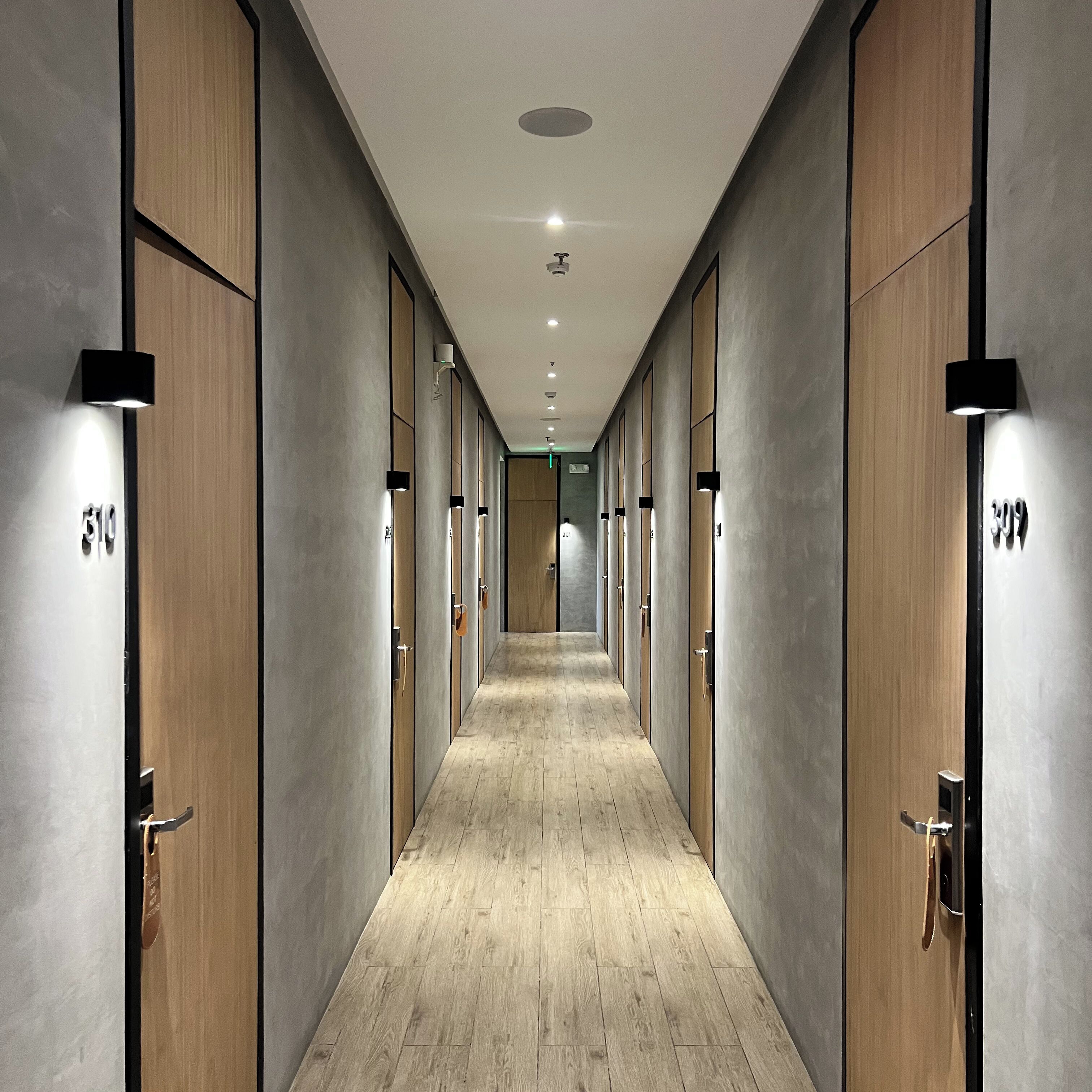 A corridor with wooden doors and a light wooden floor, leading to a room with a large window.