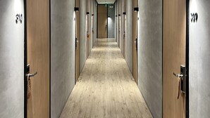 A corridor with wooden doors and a light wooden floor, leading to a room with a large window.