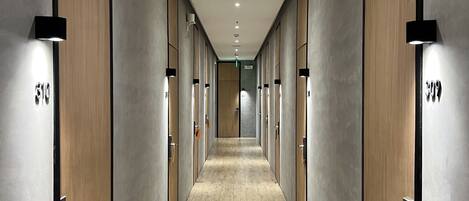 A corridor with wooden doors and a light wooden floor, leading to a room with a large window.