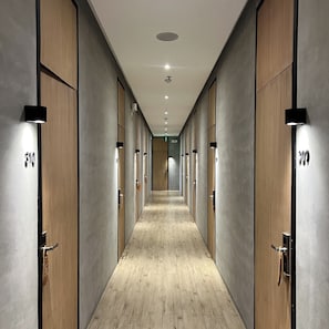 A corridor with wooden doors and a light wooden floor, leading to a room with a large window.
