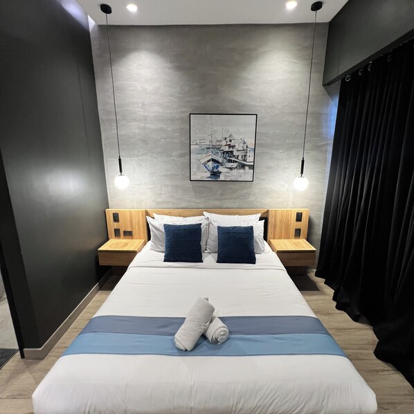 A modern hotel room with a large bed, two bedside tables, a headboard with built-in lighting, a framed picture on the wall, and a black curtain. - Caldwell Boutique Hotel (Legazpi)