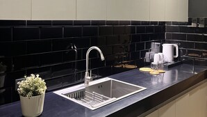 A modern kitchen with a stainless steel sink, black tiled backsplash, and a white countertop.