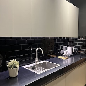 A modern kitchen with a stainless steel sink, black tiled backsplash, and a white countertop.