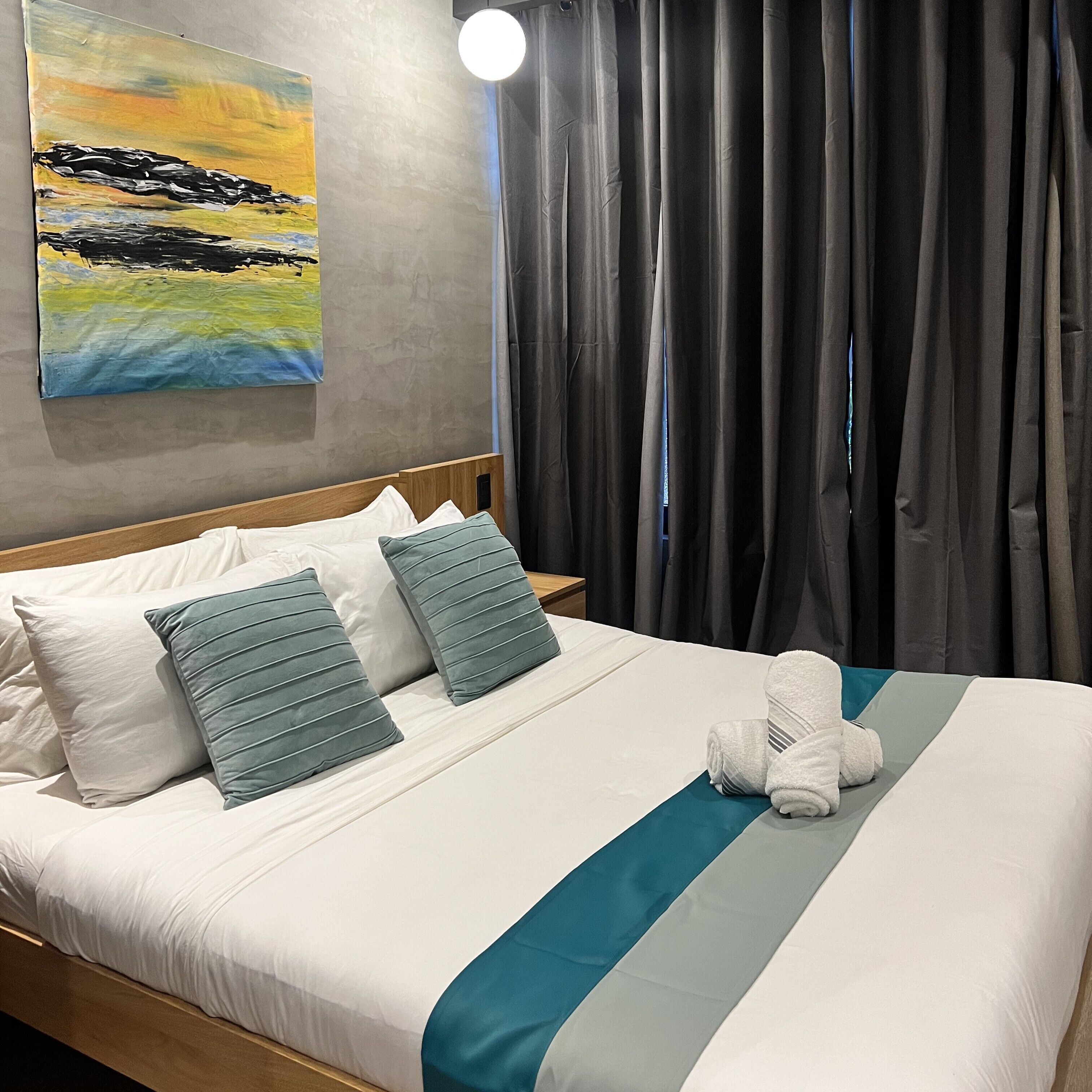 A hotel room with a bed, pillows, a blanket, and a painting on the wall.