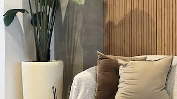 A modern living room with a sofa, a large potted plant, a lamp, and a book on a side table.