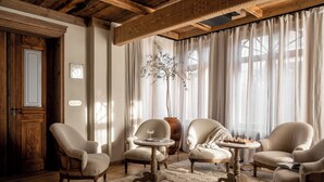 A cozy room with wooden beams, a large window with sheer curtains, and three upholstered chairs around a small table with a chessboard. - VILLA VENA (Zakopane)