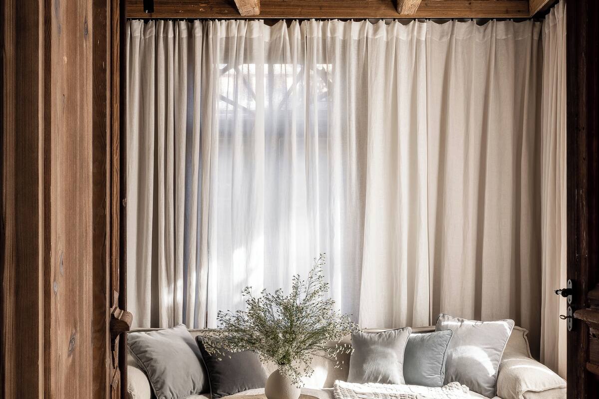 A cozy room with a wooden ceiling, a sofa with cushions, a round wooden table, and a potted plant.