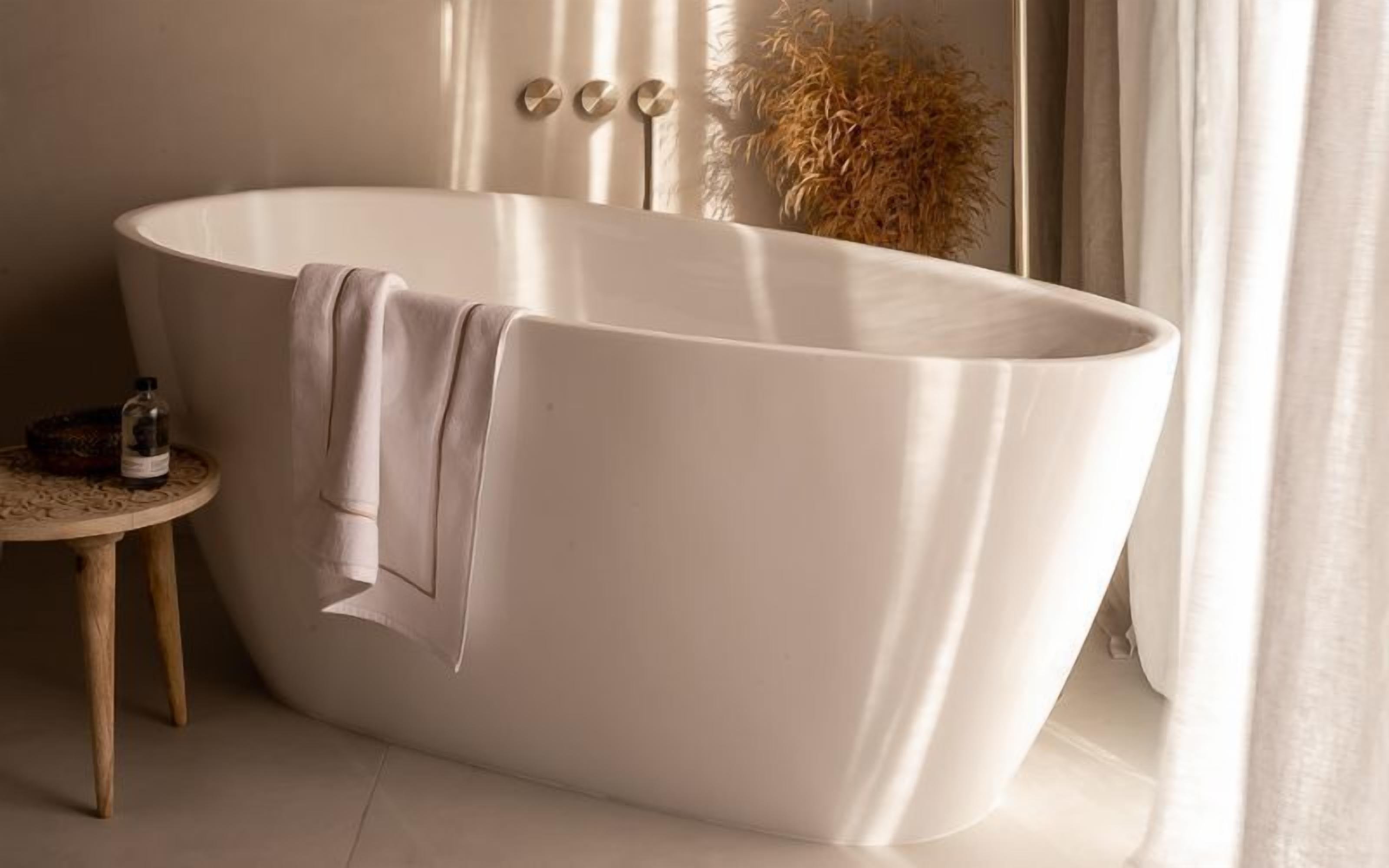 A freestanding bathtub in a bathroom with a small wooden stool and a bottle of lotion.