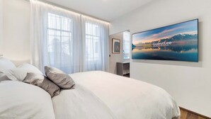 A hotel room with a large bed, a flat-screen TV on the wall, and a view of mountains through the window. - Luxury Lakefront Loft in Montreux Swiss Reviera (Territet)