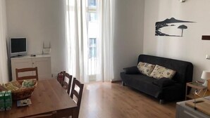 A living room with a dark sofa, a wooden dining table, and a TV on a stand.