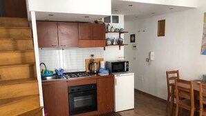 A compact kitchen with wooden cabinets, a microwave, a stove, and a small refrigerator.