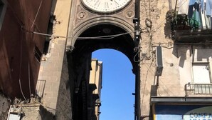 A historic archway with a large clock above it, leading to a street with buildings and parked cars. - Ale & Tizy House 2 Studio (Napoli)