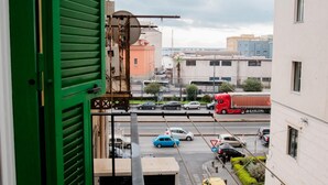 A view from a balcony overlooking a busy street with cars and a red truck, buildings in the background, and a green door partially visible. - Ale & Tizy House 2 Studio (Napoli)