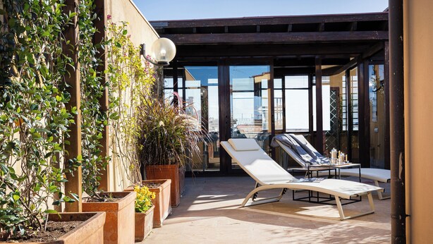 A sunlit outdoor patio with lounge chairs, potted plants, and a view of the city. - Amazing Via del Tritone (Roma)