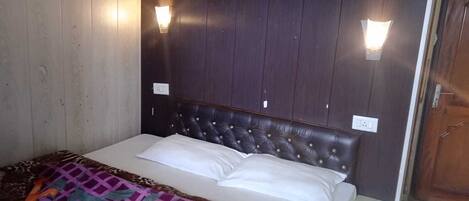 A bed with a dark headboard, two wall-mounted lights, and a patterned blanket.