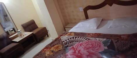 A hotel room with a bed, a small table with a lamp, a chair, and a nightstand.