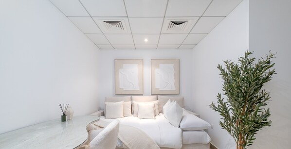Ein schlicht eingerichtetes Schlafzimmer mit einem Bett, zwei gerahmten Kunstwerken, einem Nachttisch und einer Topfpflanze.