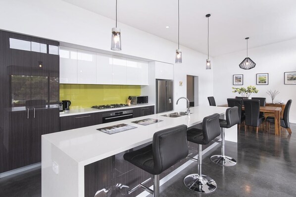 A modern kitchen with a white island, black bar stools, and a dining area with a wooden table and chairs.