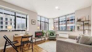 A modern living room with a sofa, a dining area with a table and chairs, a TV displaying 'NETFLIX,' and large windows with blinds. - 1 Bed Northern Quarter Loft | City Centre | Air Conditioned (Manchester)
