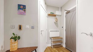 A hallway with a wooden floor, a white door, a wall-mounted shelf with plants, a wall-mounted air conditioner, and a small table with a plant. - 1 Bed Northern Quarter Loft | City Centre | Air Conditioned (Manchester)