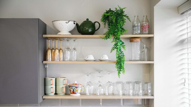 A kitchen with a sink, a green teapot, a colander, a plant, and shelves with glassware and mugs. - 1 Bed Northern Quarter Loft | City Centre | Air Conditioned (Manchester)