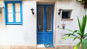 A building with a blue door, a window with blue shutters, and a small shelf with a sign.