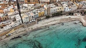 An aerial view of a coastal town with buildings along the shore and a clear turquoise sea.