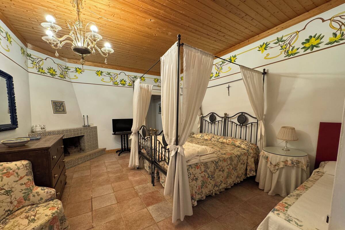 Une chambre à coucher avec un lit à baldaquin, une télévision, une petite table avec une lampe et un mur décoratif.