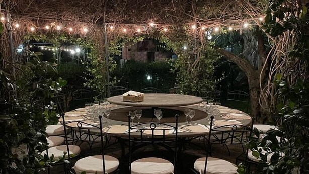 An outdoor dining area with a round table and chairs, surrounded by greenery and string lights. - Agriturismo Contrada Guido (Sellia Marina)