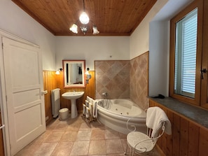 Un baño con techo de madera, una bañera, un lavamanos, un espejo y una ventana con persianas.